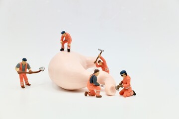 miniature figurines of men at work working on a huge human stomach - obrazy, fototapety, plakaty