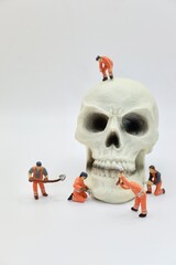 miniature figurines of men at work with a huge human skull