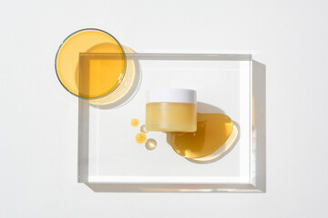 Close-up of a jar of unbranded cosmetics displayed on a transparent glass platform with drops of honey. Honey is used as a very good skin moisturizer.