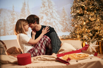 Pizza on the bed. Beautiful young couple indoors, celebrating new year against projector