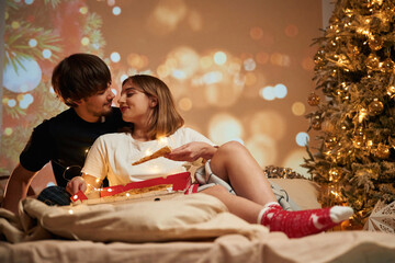 Sitting with pizza. Beautiful young couple indoors, celebrating new year against projector