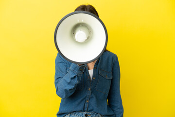Young caucasian woman isolated on yellow background shouting through a megaphone to announce...