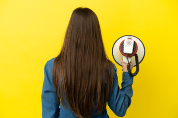 Young caucasian woman isolated on yellow background holding a megaphone and in back position