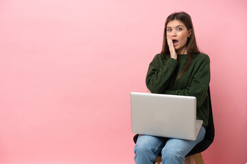 Young caucasian woman sitting on a chair with her laptop isolated on pink background surprised and shocked while looking right