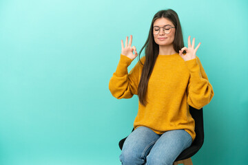 Young caucasian woman sitting on a chair isolated on blue background in zen pose