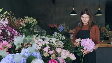 Young beautiful woman designer of floral arrangements chooses flowers for a bouquet in a flower shop. Retail sale of flowers, small business.