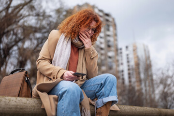 Natural portrait of a caucasian ginger woman with freckles and curly hair. She is depressed.