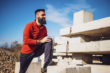 Adult man is exercising outdoor on sunny day. He is stretching his body.