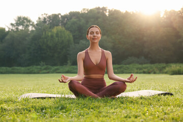 Beautiful young woman practicing Padmasana on yoga mat outdoors. Lotus pose