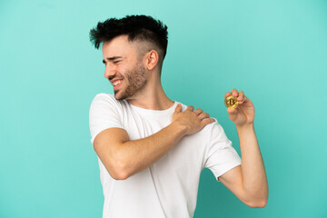 Young man holding a Bitcoin isolated on blue background suffering from pain in shoulder for having made an effort - obrazy, fototapety, plakaty