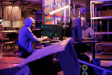 Hacker group collaborating in abandoned warehouse while hacking government server on computer. Criminals working together while coding internet virus software for data breach