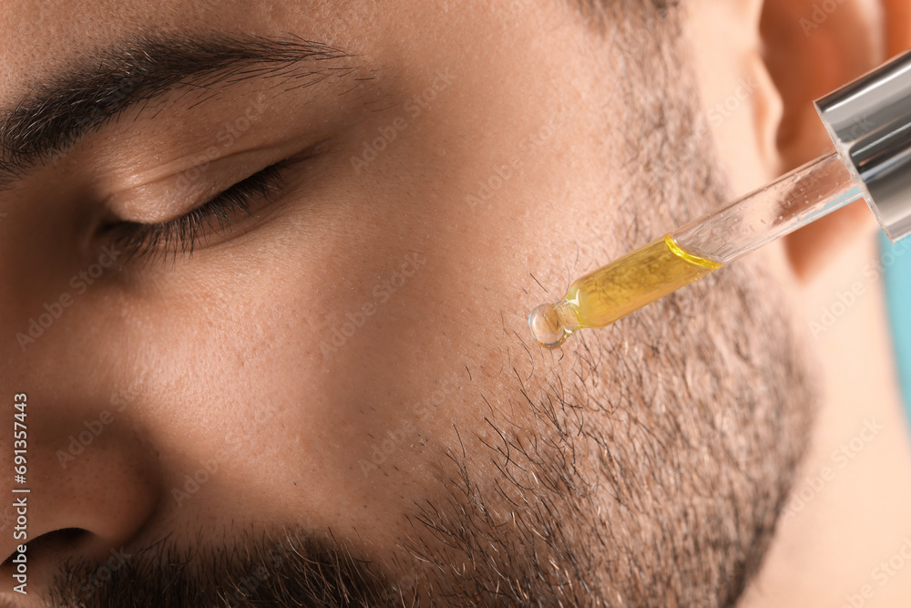 Poster Handsome man applying cosmetic serum onto face, closeup