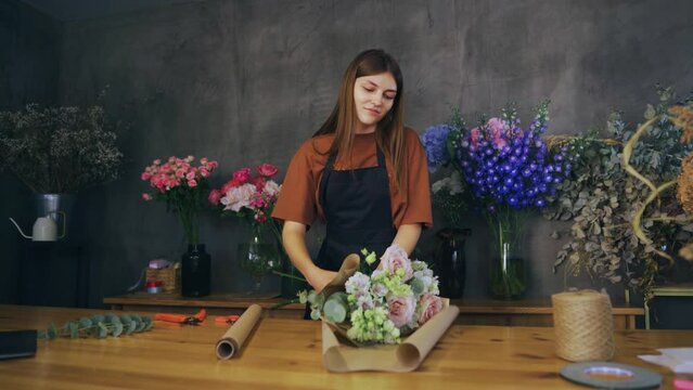Florist young woman in a flower shop cuts craft paper and wraps a bouquet. Creating a beautiful bouquet.