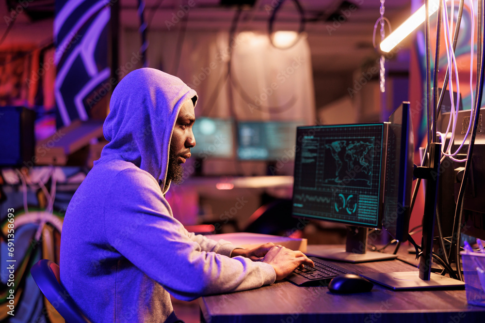 Poster african american hacker coding spyware in abandoned warehouse. man in hood using computer for breach