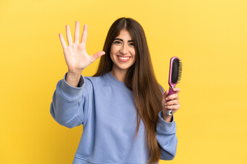Young caucasian woman holding hairbrush isolated on blue background counting five with fingers