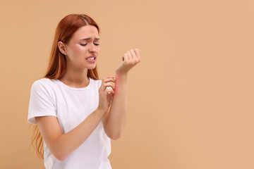 Suffering from allergy. Young woman scratching her arm on beige background, space for text