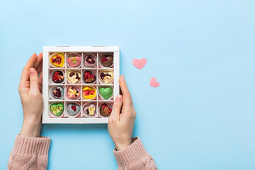 Female hands with delicious candies in box on color background