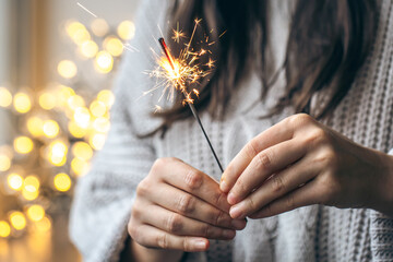 Woman with gray sweater holding a sparkling sparkler in her hands, close up.