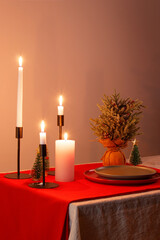 christmas table, candles, flowers, red tablecloth and plates, dim yellow light