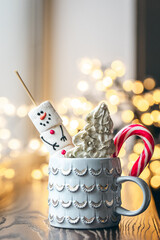 Hot drink with marshmallows, gingerbread and candy cane in mug.