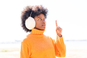 African American girl wearing winter muffs at outdoors thinking an idea pointing the finger up