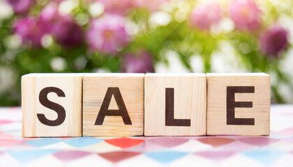 Four wooden blocks in a row saying Sale on a wooden table, with a blurry floral bokeh background. Shopping sale retail shop concept.	