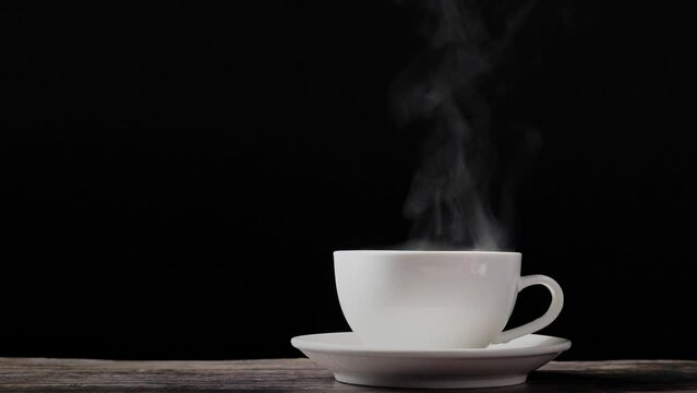 Coffee cup or tea cup with steam smoke of coffee on wooden table in black background.
