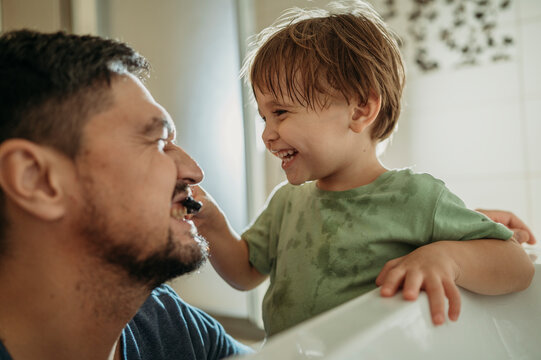 Playful boy brushing father's teeth in bathroom at home