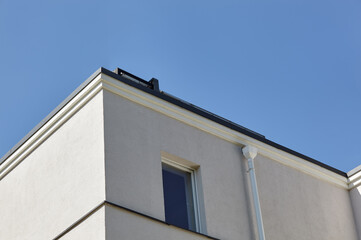 Facade of a building with downspout. Guttering and drainage pipe exterior. Old concrete wall with windows against blue sky