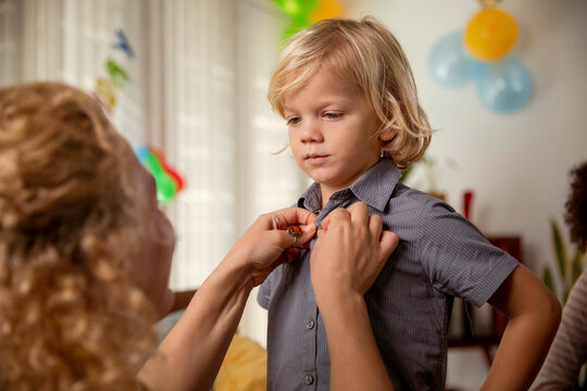 Woman helping son to button up shirt for birthday celebration