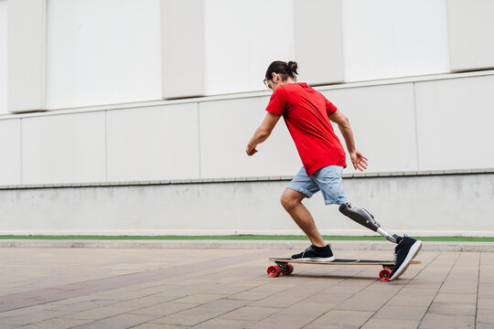 Young man with prosthetic leg riding skateboard at footpath