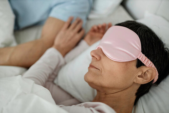 Woman wearing sleeping mask while lying in bed next to her husband