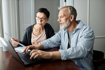 Senior couple talking about family business issues while sitting at table in front of laptop at home