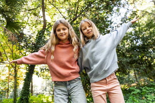 Smiling girls with arms raised standing in front of trees at park
