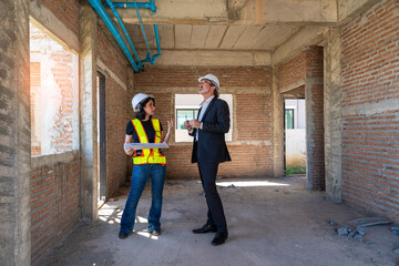 Caucasian female engineer holds blueprints and inspects work with real estate project manager in construction housing project.
