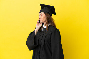 Middle aged university graduate isolated on yellow background keeping a conversation with the...