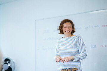 Smiling teacher standing in front of whiteboard at classroom