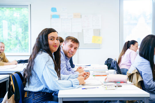 Smiling diverse friends sitting at desk with books in classroom