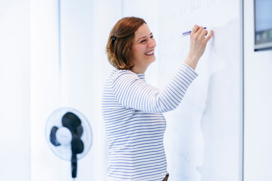 Happy teacher writing on whiteboard and teaching in classroom