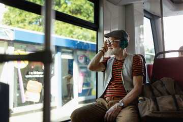 Elderly man traveling through the city by bus, listening music via modern headphones. Senior city...