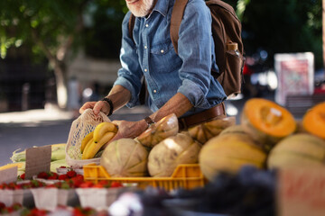 Senior man shopping at market in the city. Elderly man buying fresh vegetables and fruits from market stall.