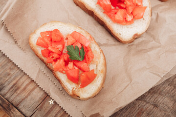 Delicious bruschetta, toasted bread with tomatoes on craft paper, on a wooden background