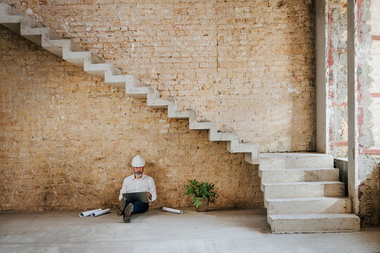 Architect using laptop and sitting under staircase at construction site