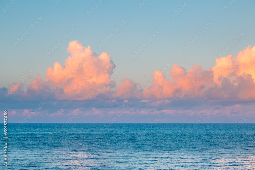 Poster Fluffy pink clouds over a calm sea at dawn.