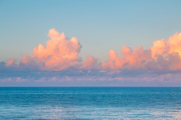 Fluffy pink clouds over a calm sea at dawn.