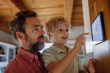 Boy helping father to adjust, lower heating temperature on thermostat. Concept of sustainable,...