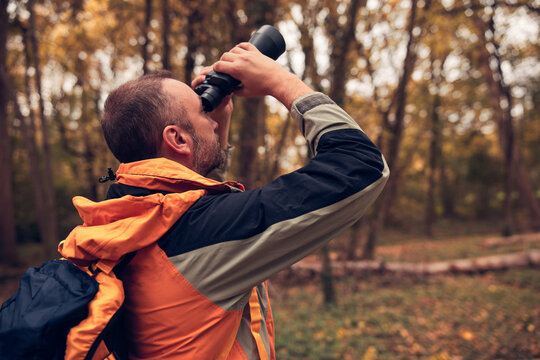 Man using binoculars and camera for bird and animal watching in nature.