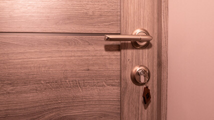 Buy Or Rent concept. Keys with trinket in shape of house in the door keyhole.