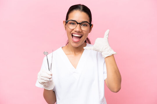 Dentist Colombian woman isolated on pink background making phone gesture. Call me back sign