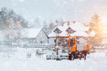 An orange truck with a salt and sand spreader clears the snow and ice from the road. The winter...